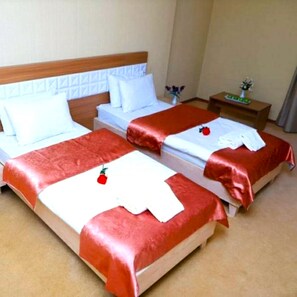 A hotel room with two beds, each with a red bedspread and white pillows. There is a nightstand with a vase of flowers and a small table with a green tray. - Gabala City Hotel (Gabala)