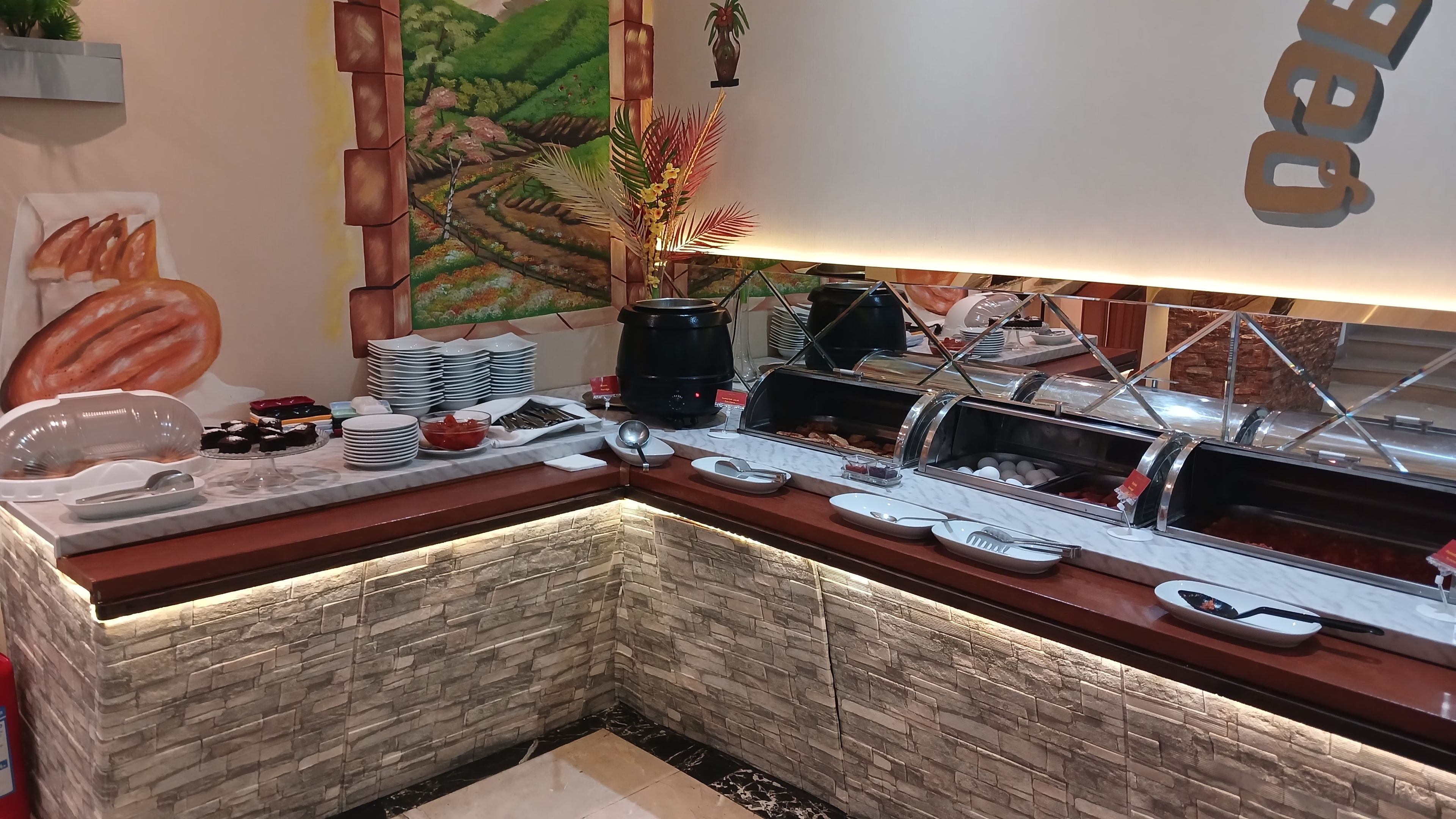Un buffet proposant une variété de plats et d’ustensiles, un mur en pierre et une fresque murale.