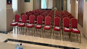 A conference room with rows of red chairs, a chandelier, and a projector screen. - Gabala City Hotel (Gabala)