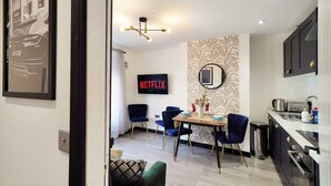 Ein modernes Wohnzimmer mit Essbereich, einer Küche und einem Wand-Fernseher, der 'NETFLIX' zeigt.
