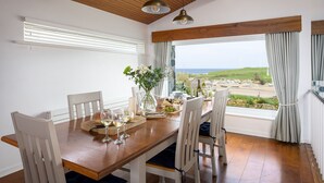 A dining area with a wooden table, white chairs, and a view of the sea.