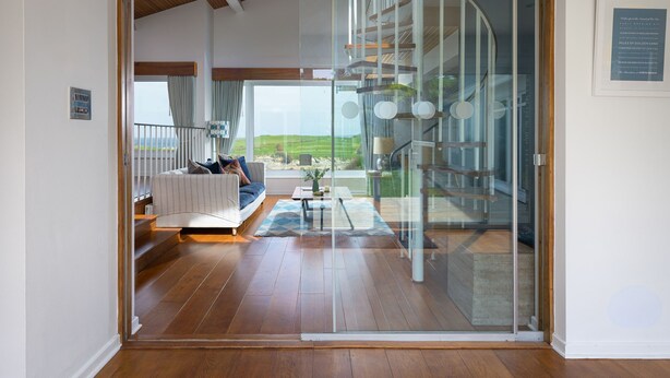 A modern interior with a glass door leading to a balcony, wooden flooring, and a seating area with a view of the outdoors.