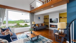 A spacious living room with a large window offering a view of the countryside, a cozy sofa set, a fireplace, and a staircase leading to an upper level.