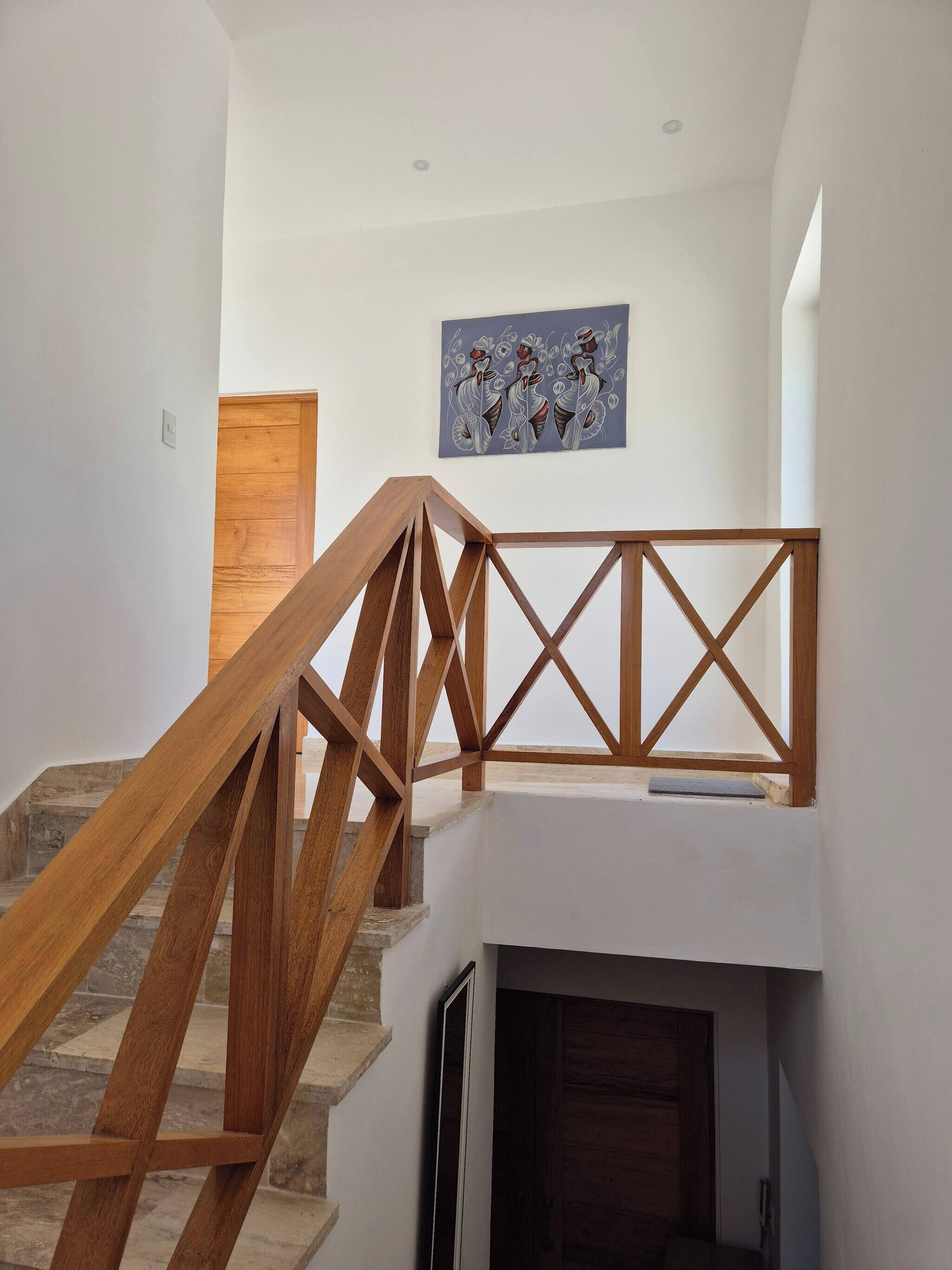 A staircase with wooden railings and a modern design, leading to a landing with a wooden door and a wall-mounted artwork.