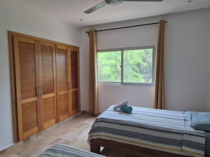 A bedroom with a bed, a wooden wardrobe, a window with curtains, and a ceiling fan. - Punta Popy 3BR Duplex With Pool, Walk to Beach (Las Terrenas)