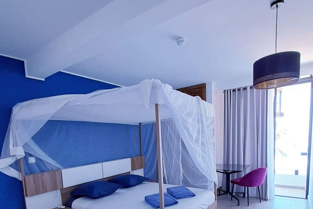 A modern bedroom with a canopy bed, a small table, a chair, and a view of the outdoors.