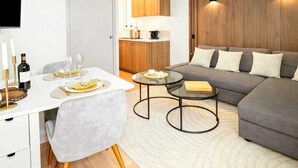En moderne stue med en grå sofa, et spisebord dækket til to personer, og et køkken i baggrunden.