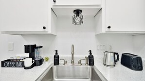 A kitchen with a stainless steel sink, a coffee bar, a kettle, a toaster, and soap dispensers. - Hyde Park Gem–Modern Studio Near UT & Downtown (Austin)