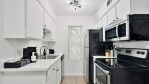 A modern kitchen with white cabinetry, a coffee bar, a microwave, a stove, and a refrigerator. - Hyde Park Gem–Modern Studio Near UT & Downtown (Austin)
