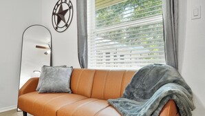 A modern living room with a leather sofa, a large mirror, and a window with blinds. - Hyde Park Gem–Modern Studio Near UT & Downtown (Austin)