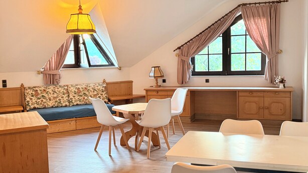 A cozy room with a wooden desk, a dining table, a sofa, and a window with curtains. - In & Out boarding house comfort for four XL rooms (Stolberg)