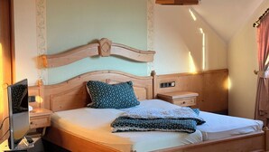 A neatly made bed with a wooden headboard, a bedside table with a lamp, and a wall with a floral pattern. - In & Out boarding house comfort for four XL rooms (Stolberg)
