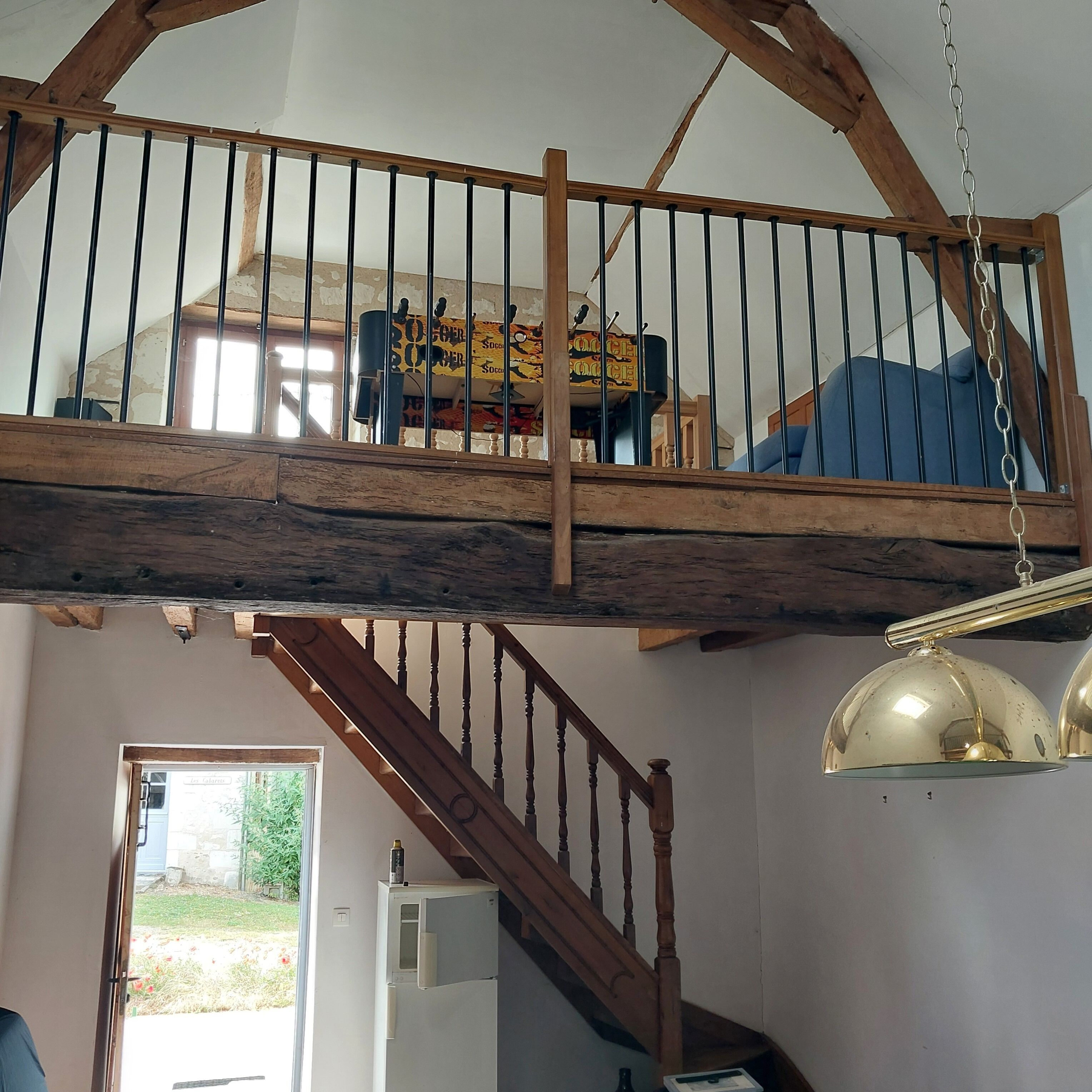 Een loft-achtige kamer met een houten trap, een hanglamp en uitzicht op de achtertuin.