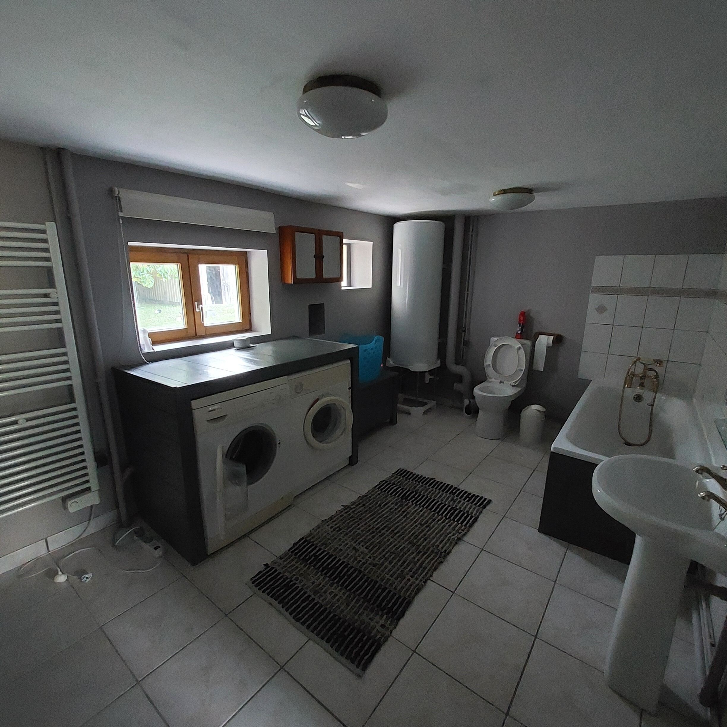 A compact bathroom with a washing machine, toilet, sink, and a small window.