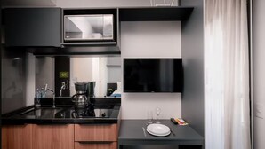 Eine moderne Küche mit schwarzem Arbeitsplatz, einer Kaffeemaschine, einer Mikrowelle und einer kleinen Essecke mit Teller, Glas und Fernbedienung.
