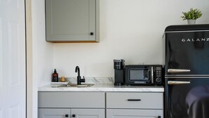 Eine Küche mit einem schwarzen Galanz-Kühlschrank, einer Mikrowelle, einer Kaffeemaschine und einem kleinen Topfpflanzen auf der Arbeitsplatte.