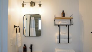 Ein Badezimmer mit einem weißen Waschbecken, einem Spiegel, einem Handtuchhalter, einem Ablagefach für Toilettenartikel und einer Toilette.