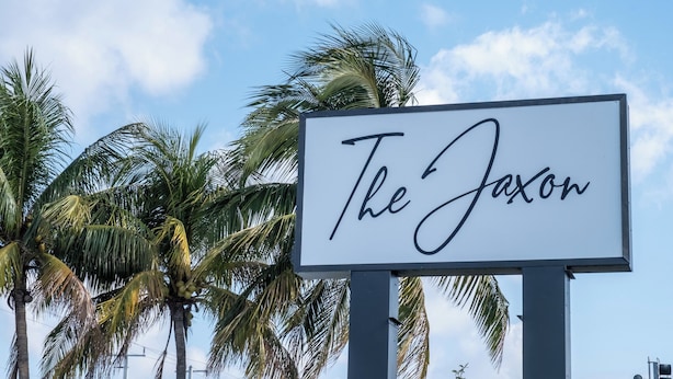 Une enseigne portant l’inscription « The Jaxon », avec en arrière-plan des palmiers et un ciel dégagé.