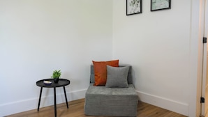 Une pièce d’angle avec un canapé gris, deux coussins, une petite table ronde ornée d’une plante, et deux œuvres d’art encadrées accrochées au mur.