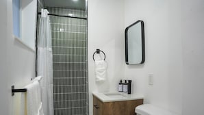 A bathroom with a shower, a toilet, a sink, and a mirror. - Comfort Living 2BR Deluxe Suite (West Palm Beach)