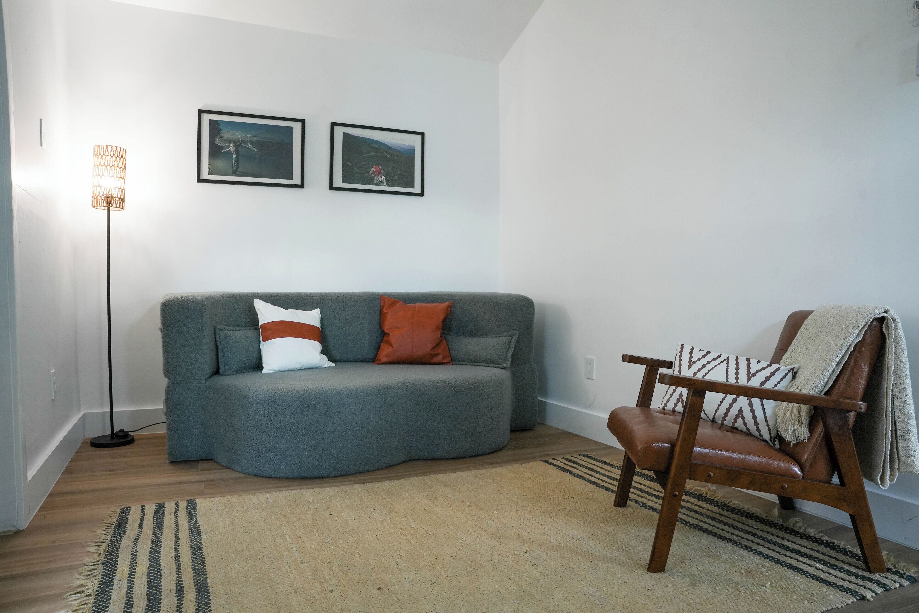 Un salon avec un canapé gris, un fauteuil en bois, deux tableaux encadrés au mur et une lampe sur pied.