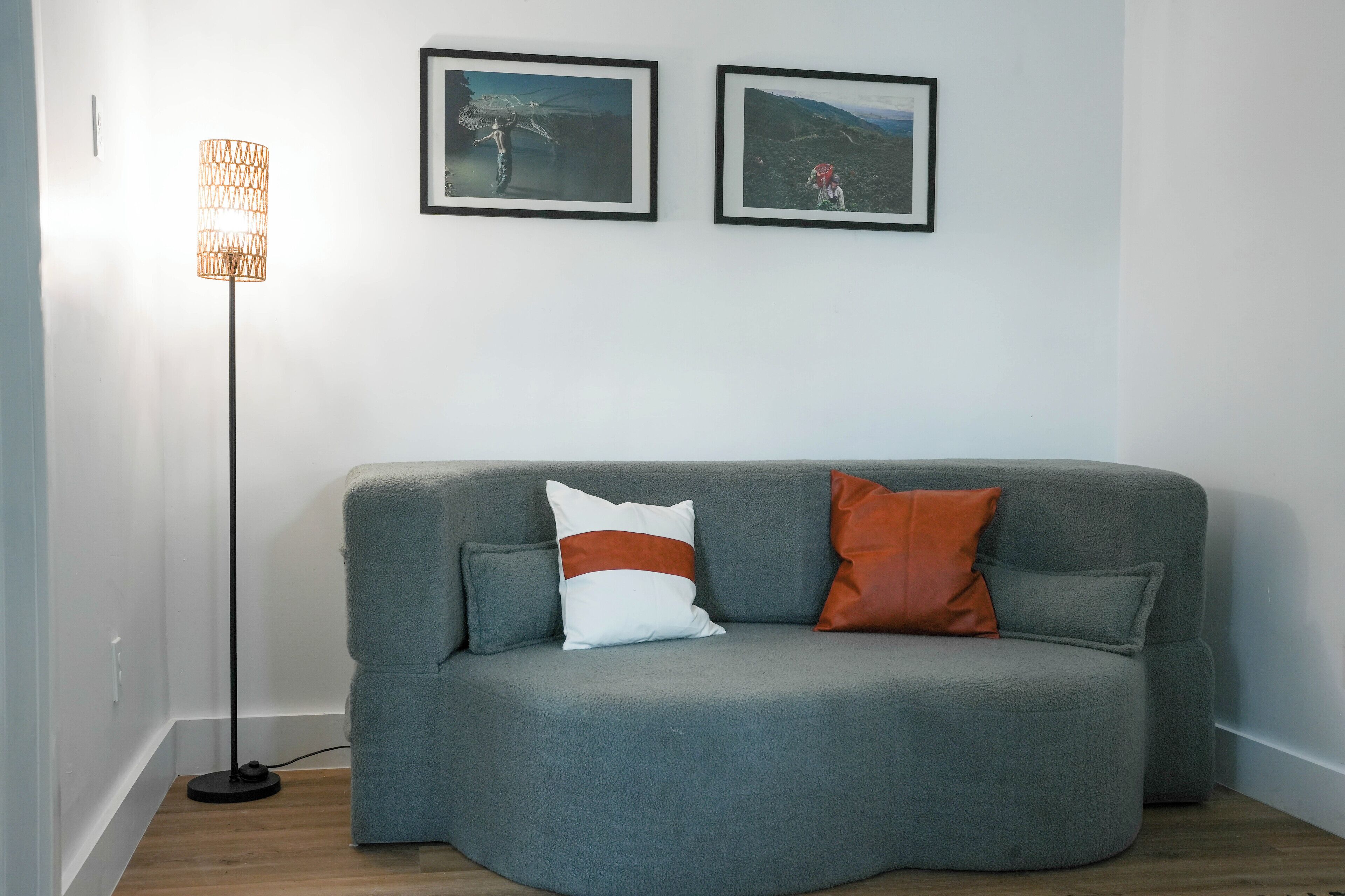 Ein graues Sofa mit zwei Kissen, einer Stehlampe und zwei gerahmten Bildern an der Wand.
