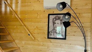 A wooden cabin interior with a wooden staircase, a white sofa, and a framed picture on the wall.