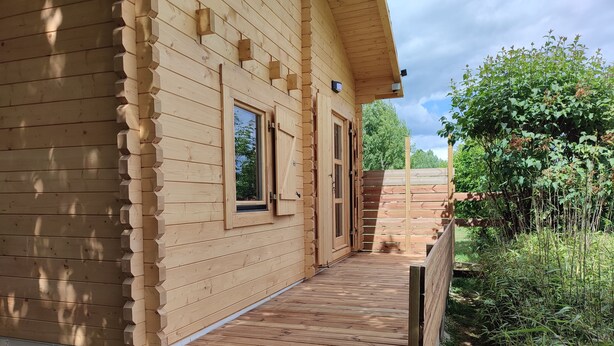 A wooden cabin with a wooden deck, a door, and a window.