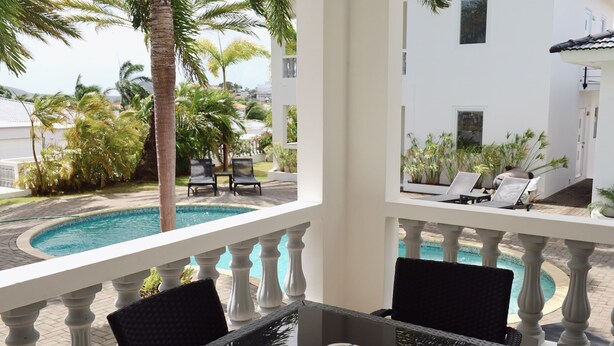 Un balcón con piscina, barandillas blancas y sillones de descanso.
