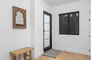 Ein Korridor mit einer hölzernen Bank, einer Tür mit Fensterglas, einem Fenster in schwarzem Rahmen und einem gemusterten Teppich.