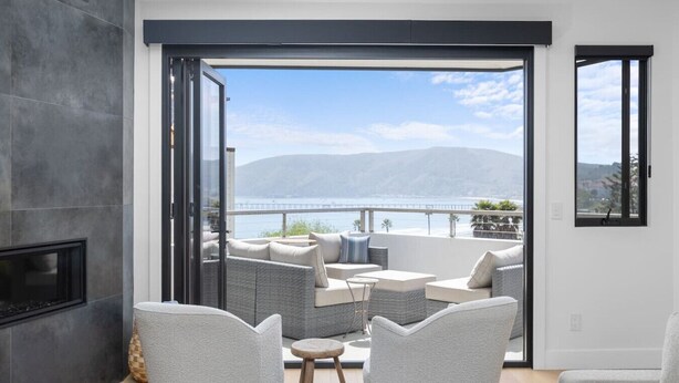 A modern living room with a fireplace, a sofa set, and a view of the sea and mountains. - Hummingbird House — Private Rooftop Terrace, Panoramic Ocean & Pier Views, 2BR/2BA Luxury Home · Steps to Avila Beach · Fireplace · Gourmet Kitchen · Beach Gear & Bikes Included · Sleeps 5 · Managed by Solmaré Stays (Avila Beach)