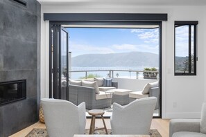 Een moderne woonkamer met een open haard, een zithoek en uitzicht op zee en bergen.