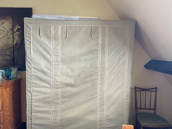 A room with a large, light-colored, striped curtain, a wooden cabinet, a chair, and a painting on the wall.