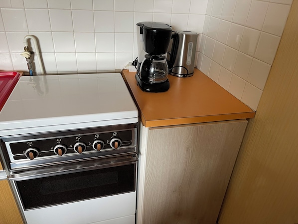 Een kleine keuken met een fornuis, oven en koffiezetapparaat op een aanrecht.