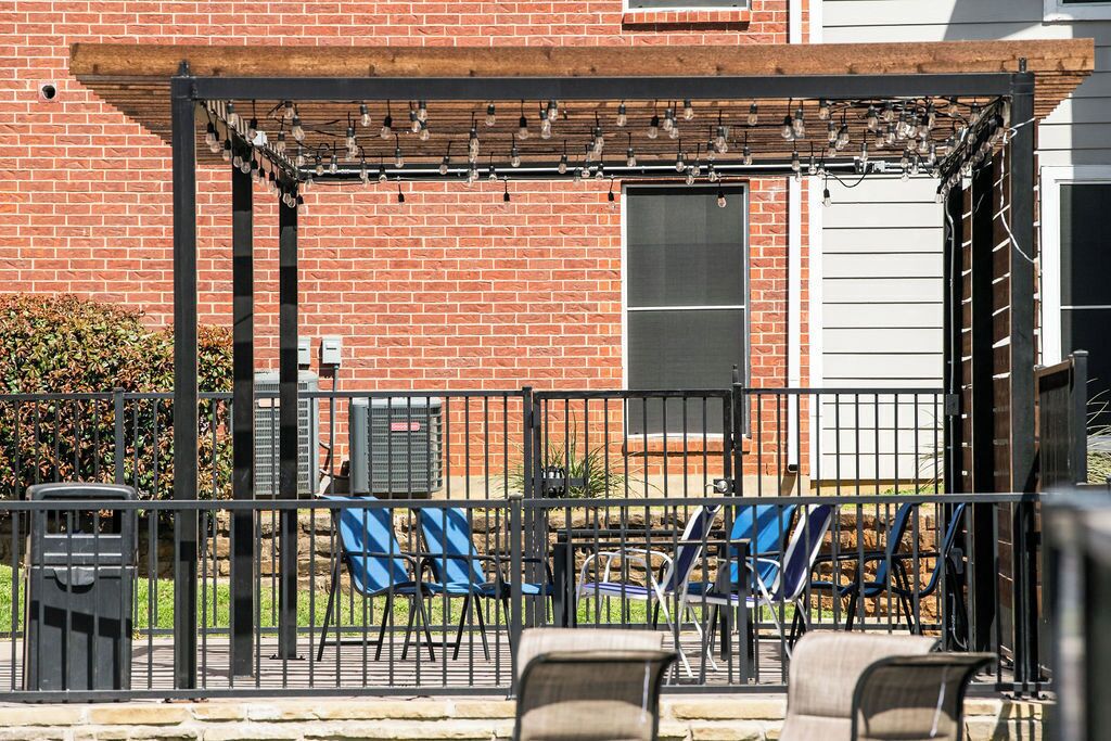 A patio area with a brick wall, a pergola with string lights, and several chairs.