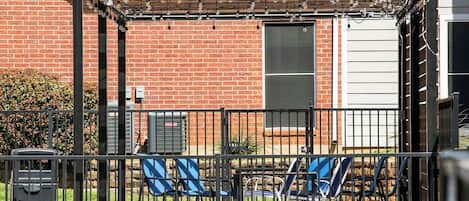 A patio area with a brick wall, a pergola with string lights, and several chairs.