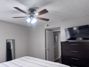 Een slaapkamer met plafondventilator, een bed, een dressoir en een televisie.