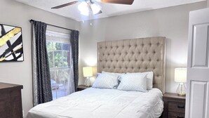 A bedroom with a tufted headboard, a bed with white bedding, two bedside lamps, and a ceiling fan. - I012 - Upgraded 2BD | Pool | DFW South 183/161 (Irving)