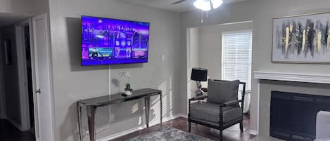 A living room with a television, a fireplace, a ceiling fan, and a decorative painting.