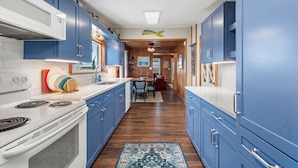 A kitchen with blue cabinets, a white stove, and a wooden floor. - The Barn: Private Pool | Hot Tub (Kill Devil Hills)
