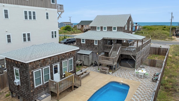 A residential area with a swimming pool, wooden deck, and multiple houses with attached porches. - The Barn: Private Pool | Hot Tub (Kill Devil Hills)