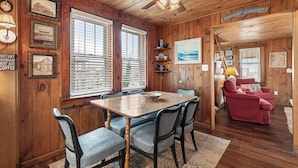 A wooden interior with a dining table, chairs, a red sofa, and a ceiling fan. - The Barn: Private Pool | Hot Tub (Kill Devil Hills)