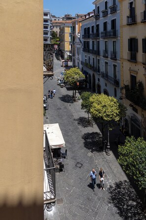 A cobblestone street with buildings on either side, outdoor seating, and a tree providing shade. - Dimora di Mare (Salerno)
