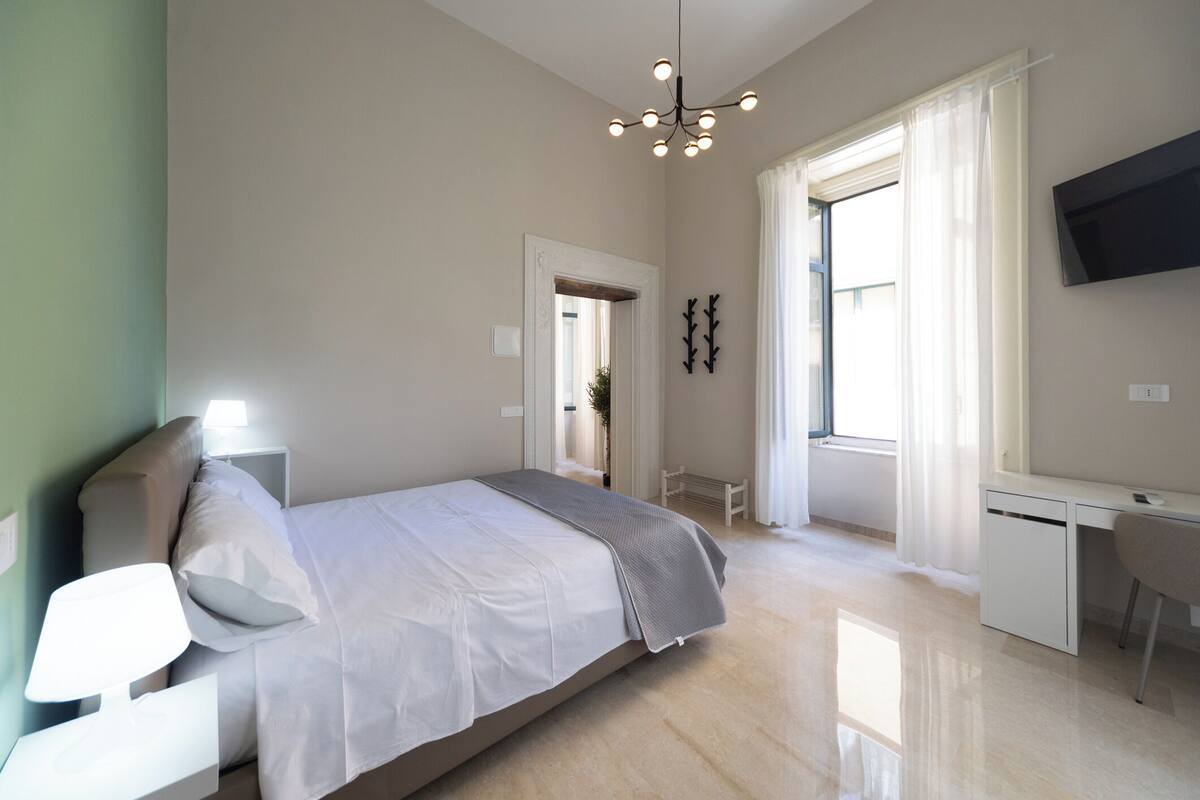 Un dormitorio moderno con cama, mesita de noche, escritorio y televisor en la pared.
