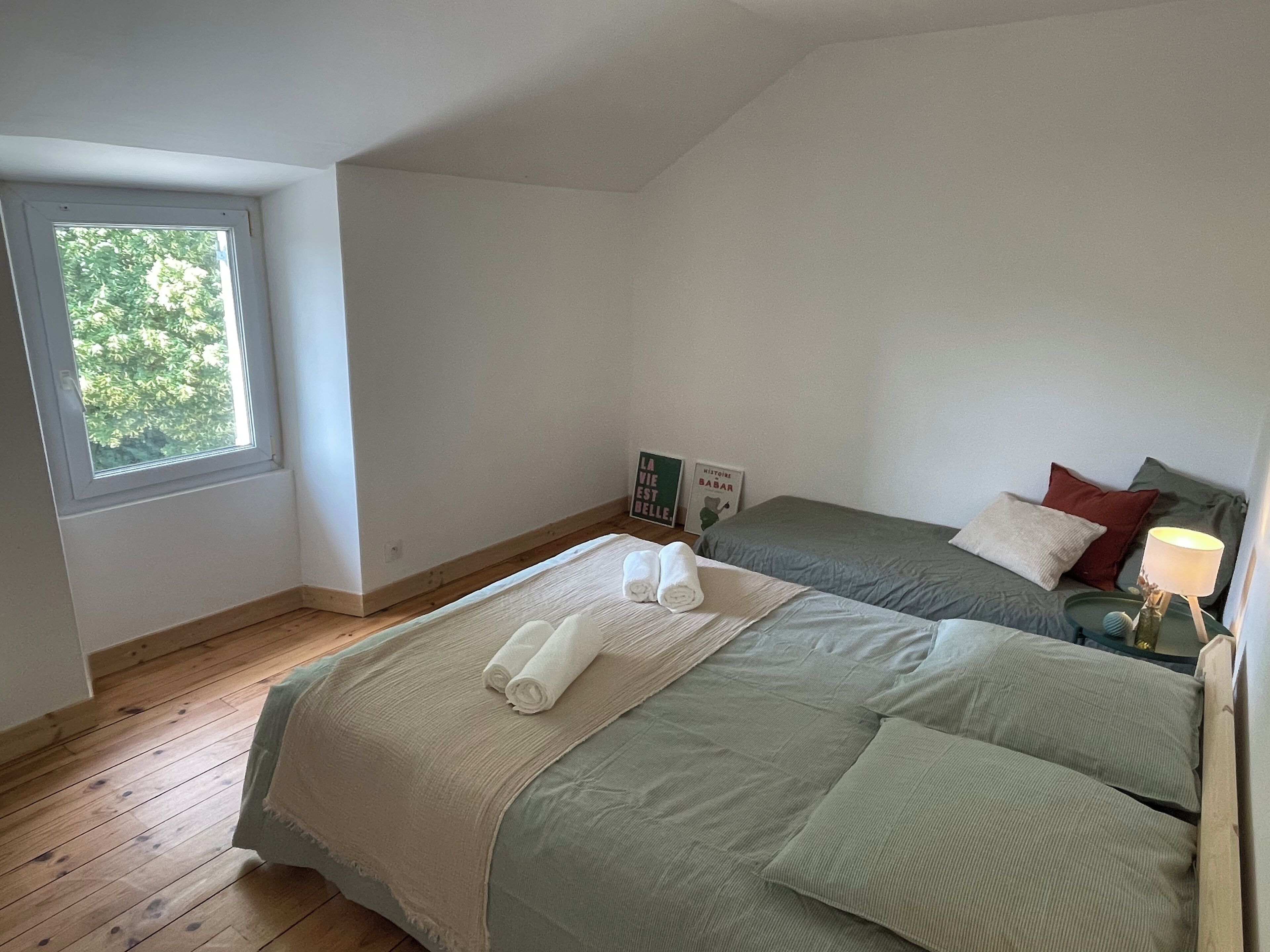 A bedroom with two beds, a window, and a bedside table with a lamp.