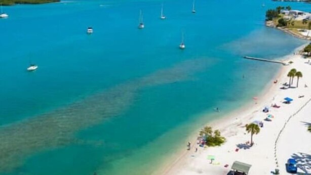A beach with clear turquoise water, several boats, and a sandy shore with umbrellas and palm trees. - Beaches/Golf - Coastal Retreat w Chefs Kitchen (Port St. Lucie)