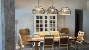 A dining area with a wooden table and chairs, three hanging pendant lights, and a window with white frames. - Beaches/Golf - Coastal Retreat w Chefs Kitchen (Port St. Lucie)