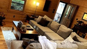 A cozy log cabin interior with a sofa, a coffee table, and a lamp. - Peaceful Cabin: Trails, Winery, Fire-pit & 12 Acr (Newland)