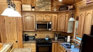 A compact kitchen with wooden cabinets, a microwave, stove, and a sink. - Peaceful Cabin: Trails, Winery, Fire-pit & 12 Acr (Newland)