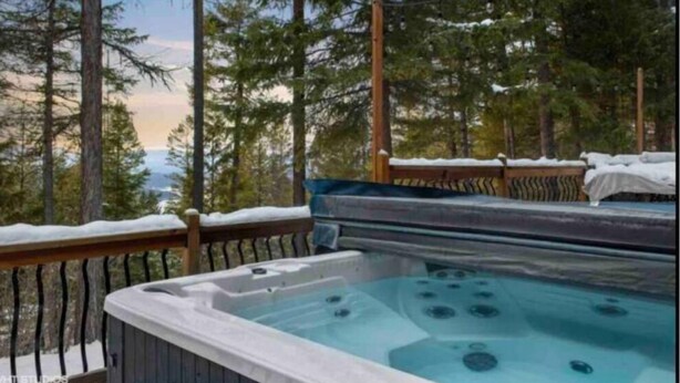 A hot tub on a wooden deck with snow on the railings, surrounded by tall pine trees. - Peaceful Cabin: Trails, Winery, Fire-pit & 12 Acr (Newland)